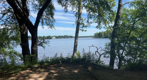 A serene view of a lake framed by trees under a blue sky with scattered clouds.
