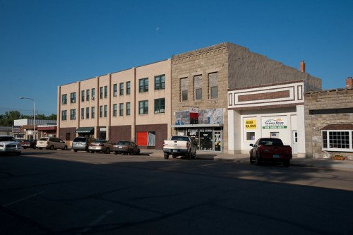 A street view of a small town featuring brick buildings and parked cars under a clear blue sky.
