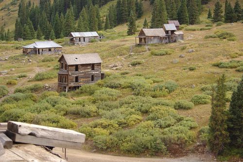 Abandoned wooden buildings on a hillside surrounded by greenery and trees.