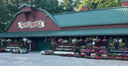 A red barn-style building with a green roof, adorned with colorful flower baskets and a welcoming sign.