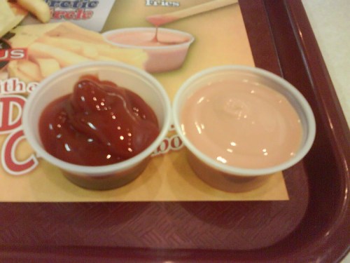 Two small cups on a tray: one filled with ketchup and the other with a pink dipping sauce.