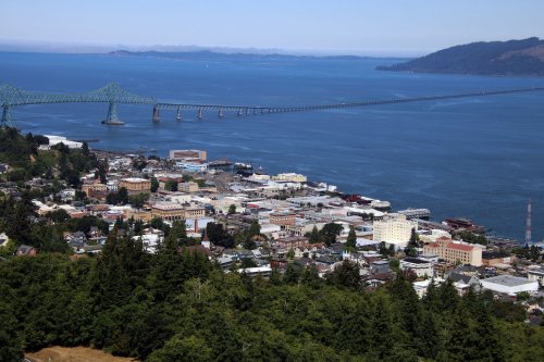 Aerial view of a coastal town with a bridge over water, surrounded by trees and mountains in the background.