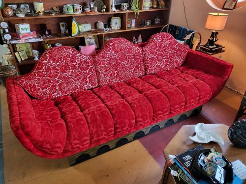 A vibrant red vintage sofa with a unique curved design, set in a cozy room filled with eclectic decor.