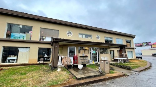 A two-story building with large windows, displaying various items outside, set against a cloudy sky.