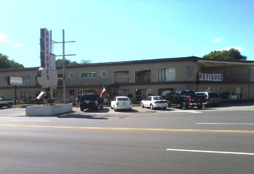 A vintage antique store with a large sign, featuring several parked cars and a clear blue sky in the background.