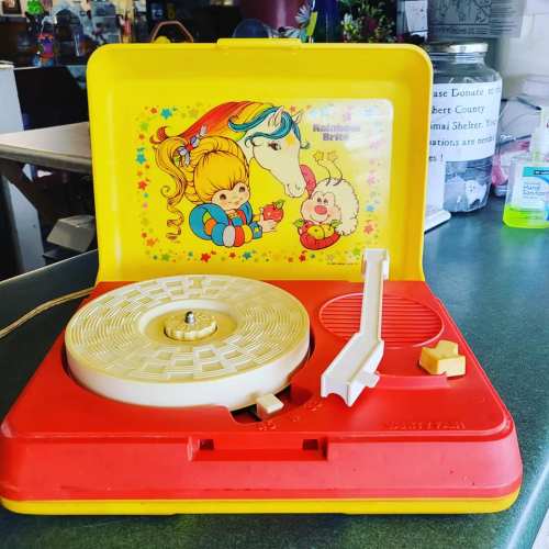 A vintage toy record player in bright colors, featuring a playful design with children and a horse on the lid.