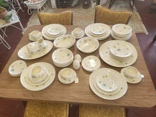 A wooden table set with a complete vintage dishware collection featuring floral patterns.