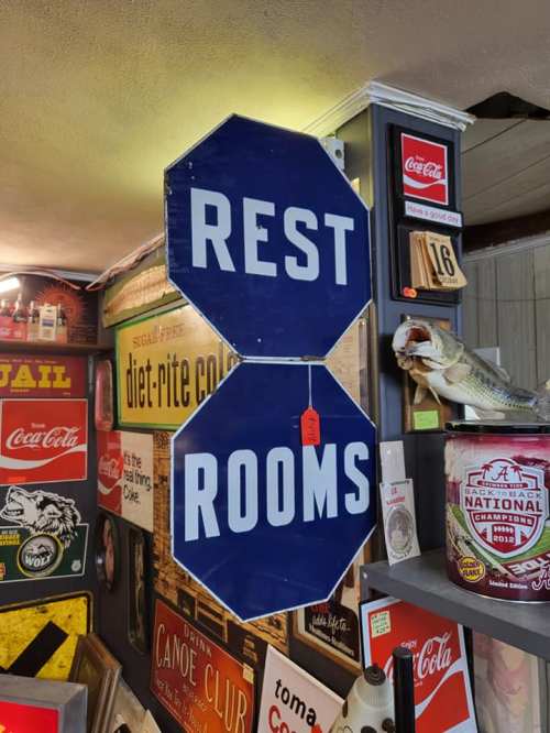 A blue octagonal sign with white text reading "REST ROOMS," hanging in a vintage-themed space.
