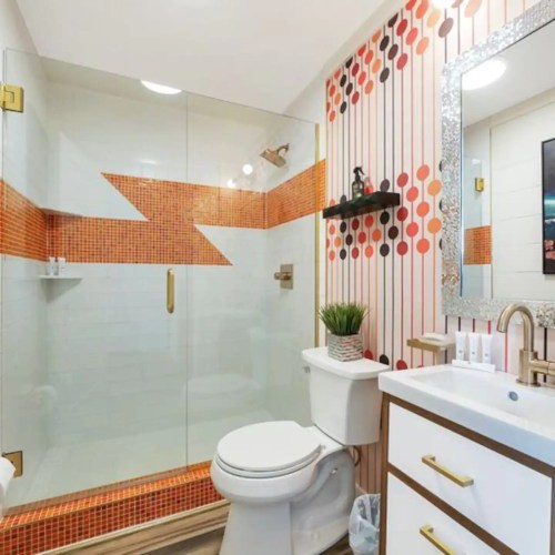 A modern bathroom featuring a glass shower, orange mosaic tiles, and a stylish vanity with a mirror.