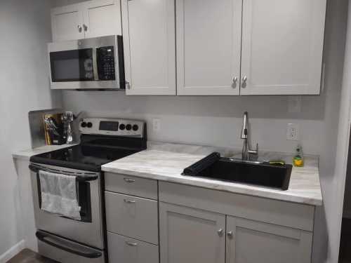 Modern kitchen featuring stainless steel appliances, a marble countertop, and a black sink with white cabinets.