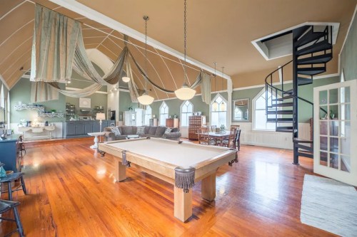 Spacious room with a pool table, spiral staircase, and elegant decor featuring large windows and wooden floors.