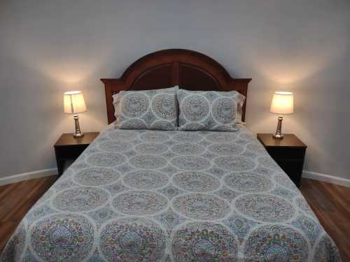 A neatly made bed with a patterned comforter, flanked by two bedside lamps in a softly lit room.