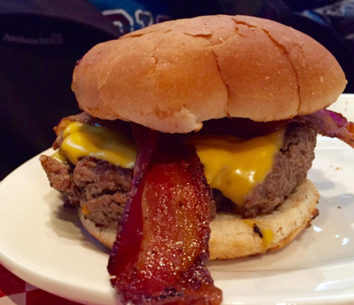 A close-up of a cheeseburger with bacon on a toasted bun, served on a white plate.