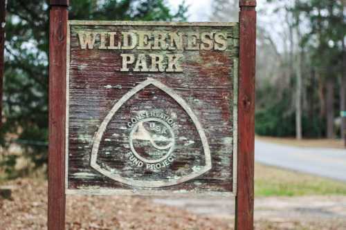 Weathered sign for Wilderness Park, featuring a conservation emblem and surrounded by trees.