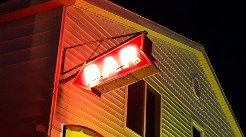 A glowing red "BAR" sign illuminated at night, mounted on the side of a building.