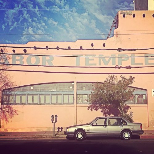 A silver car parked in front of a pink building with "Labor Temple" painted on the wall under a blue sky.