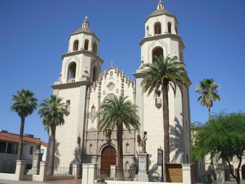 Historic church with twin towers, palm trees, and intricate architectural details against a clear blue sky.