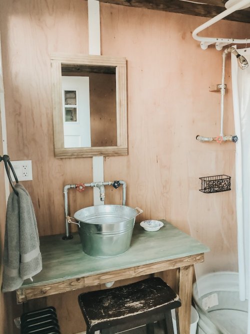 A rustic bathroom with wooden walls, a mirror, a metal bucket on a table, and a shower curtain.