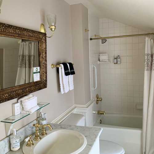 A bathroom featuring a bathtub, shower curtain, ornate mirror, and marble countertop with toiletries.