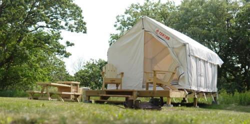 A white canvas tent on a wooden platform, surrounded by greenery, with outdoor seating and a picnic table nearby.