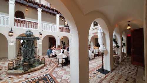 A spacious indoor courtyard with arches, a fountain, and dining areas filled with people enjoying their meals.