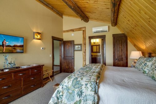 Cozy bedroom with wooden beams, a TV, and a floral bedspread, featuring warm lighting and rustic decor.