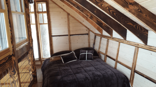 Cozy attic bedroom with a sloped wooden ceiling, a large bed, and natural light from windows.