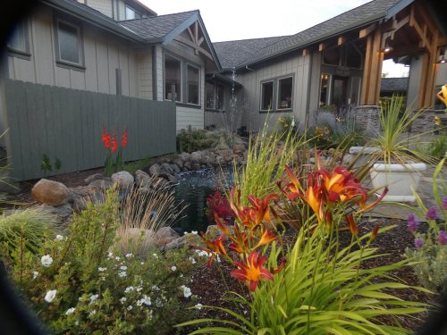 A landscaped garden with colorful flowers, a pond, and a modern house in the background.