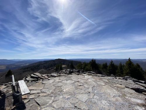 A scenic view from a rocky overlook, featuring distant mountains and a clear blue sky with wispy clouds.