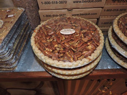 Two pecan pies stacked on a table, with a label on top, surrounded by boxes in the background.