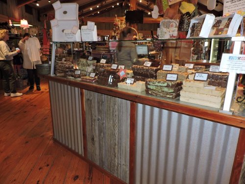 A display case filled with various types of fudge in a cozy shop, with customers browsing in the background.