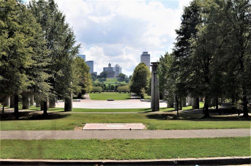 A park view with trees, pathways, and a skyline in the background under a partly cloudy sky.