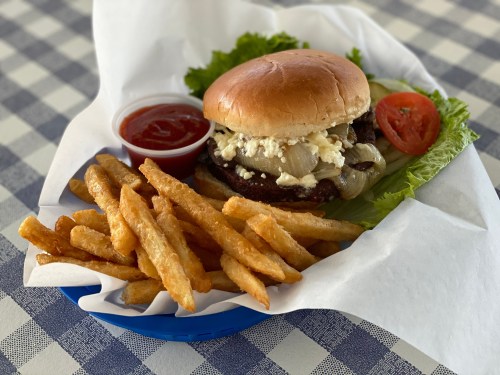 A burger with lettuce, tomato, and onions, served with crispy fries and a side of ketchup on a checkered tablecloth.