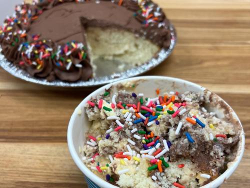 A bowl of cake with colorful sprinkles in front of a chocolate frosted cake with a slice cut out.