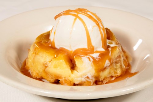 A warm dessert featuring a slice of cake topped with vanilla ice cream and drizzled with caramel sauce.