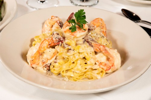 A plate of fettuccine pasta topped with shrimp and a creamy sauce, garnished with a sprig of parsley.