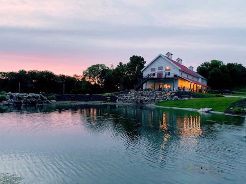 A serene lakeside view of a white house with a red roof, reflecting in the water at sunset.
