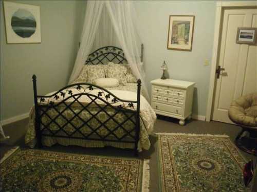 Cozy bedroom featuring a wrought iron bed, decorative rugs, and soft lighting with a nightstand and artwork on the walls.