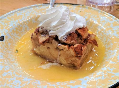 A slice of bread pudding topped with whipped cream, served on a colorful plate with a drizzle of sauce.
