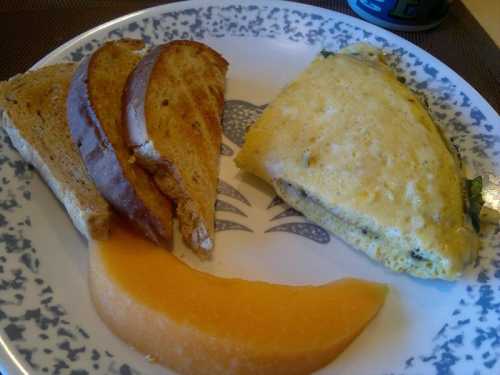 A plate with an omelette, two slices of toast, and a wedge of cantaloupe.