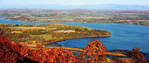 A scenic view of a river winding through vibrant autumn foliage and rolling hills under a clear blue sky.