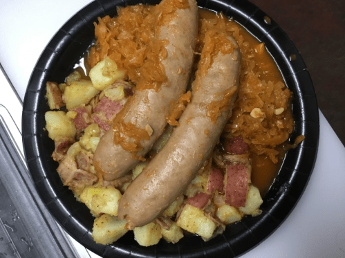 A black plate with two sausages, sauerkraut, and seasoned diced potatoes.