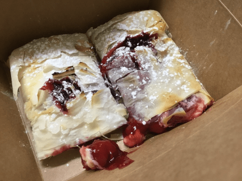Two pieces of flaky pastry filled with cherry filling, dusted with powdered sugar, in a cardboard box.