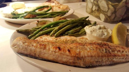 Grilled fish fillet with green beans, zucchini, and a side of tartar sauce and lemon on a white plate.