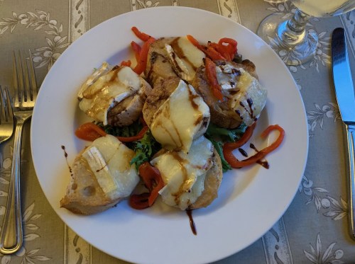 A plate of baked bread topped with cheese, red peppers, and a drizzle of sauce, served on a decorative tablecloth.