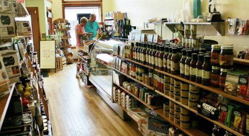 A cozy grocery store aisle with shelves of products and two customers at the counter.