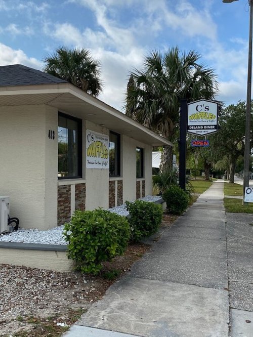 Exterior of C's Waffles diner with a sign, palm trees, and a sidewalk in a sunny setting.
