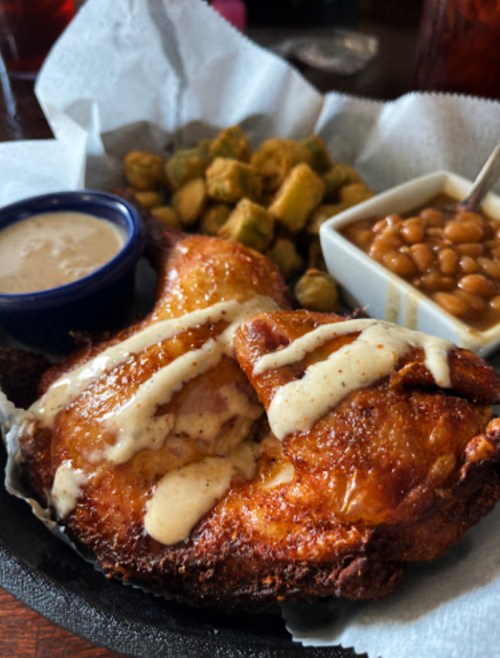 A plate of fried chicken with white sauce, sides of okra and baked beans, served in a casual dining setting.