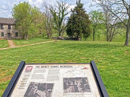 Sign for the Nancy Hanks Memorial in a grassy area, with trees and a historic building in the background.