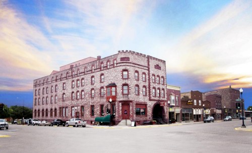 Historic brick building at a street corner, with a sunset sky and parked cars in the foreground.